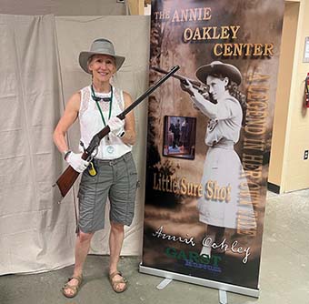 Woman holding a rifle next to a poster of Annie Oakley