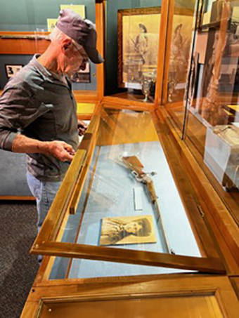 Photo of a man opening a display case and removing Annie Oakley's rifle