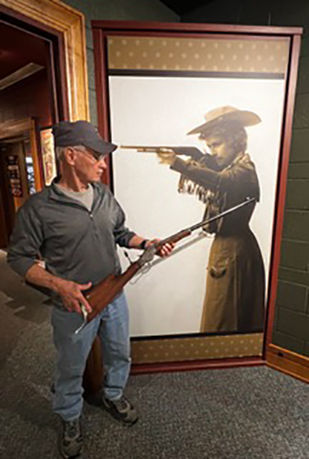 Man holding Annie Oakley's rifle in front of a large photo of Annie.